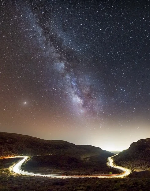 Una strada fra le montagne con una vista spettacolare sul cielo in cui si vede la via lattea