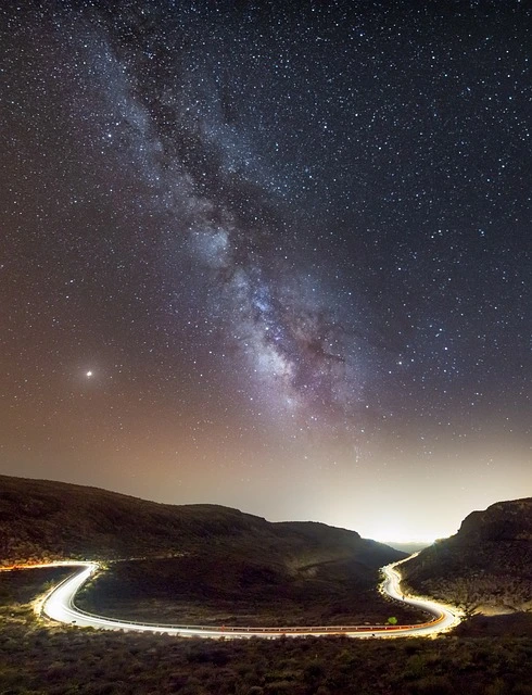 Una strada fra le montagne con una vista spettacolare sul cielo in cui si vede la via lattea